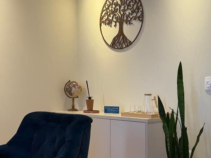 Poltrona azul, aparador e quadro decorativo em formato de árvore no consultório